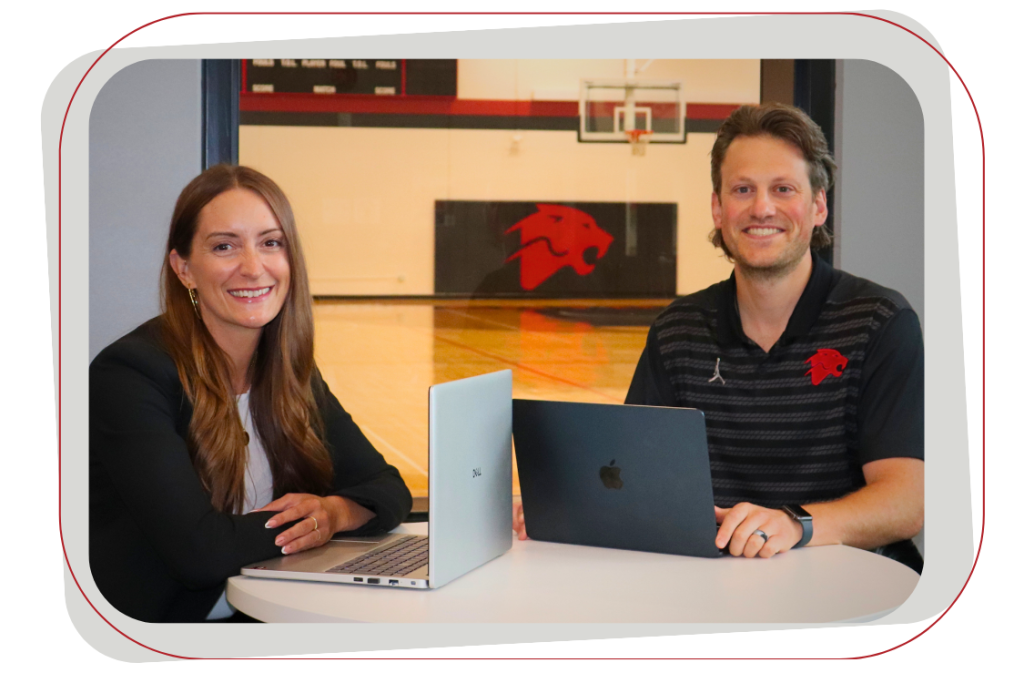 two people at a table with laptops smiling at the camera